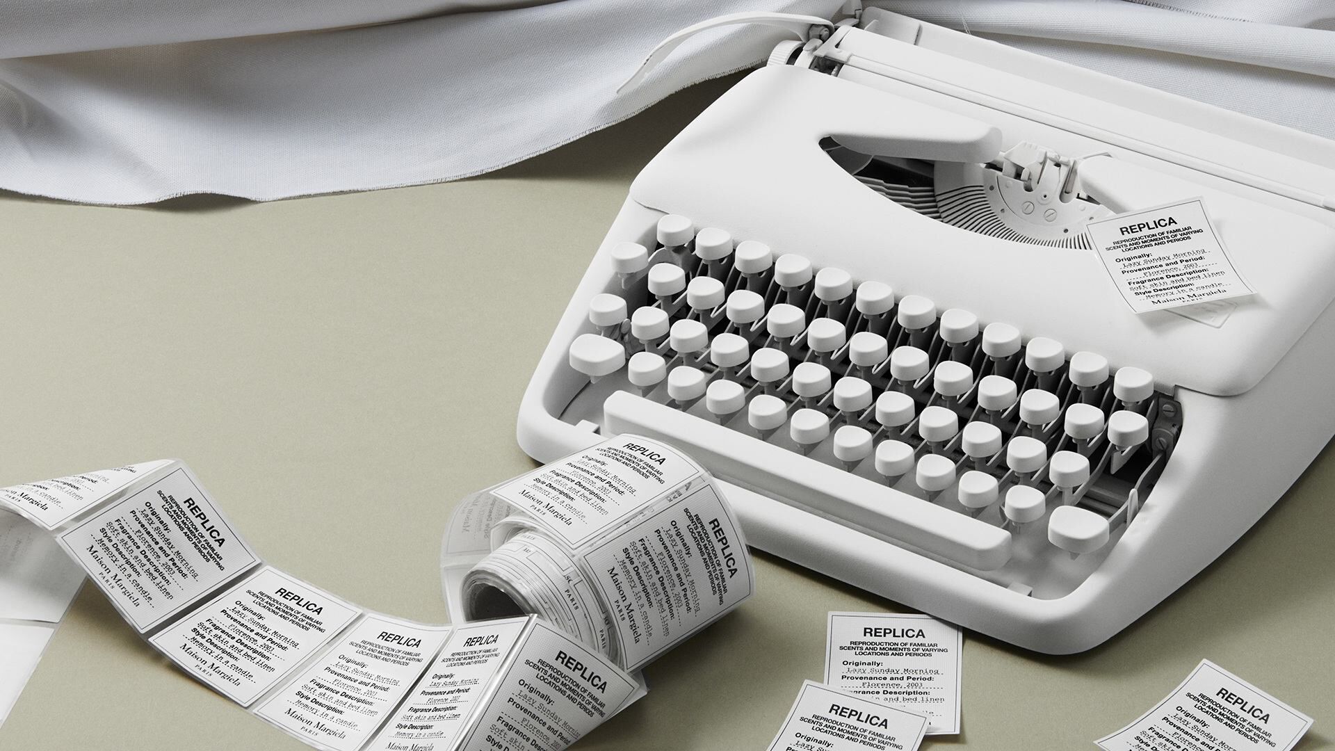 White typewriter with rolls and loose Maison Margiela Replica fragrance labels.